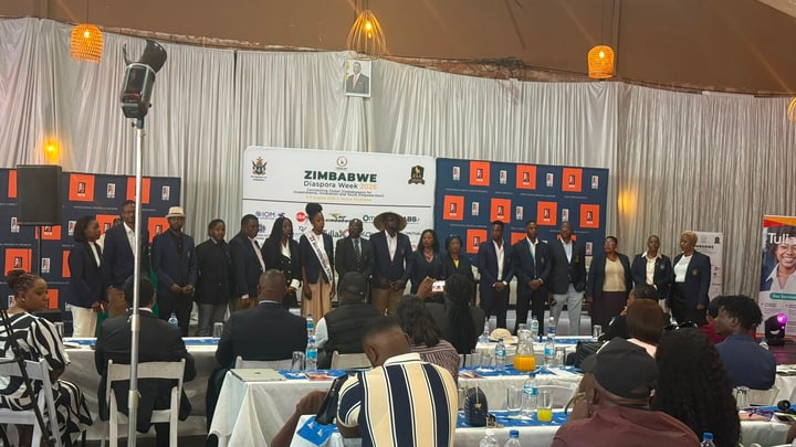 Participants stand on stage while guests are seated at tables in the foreground.